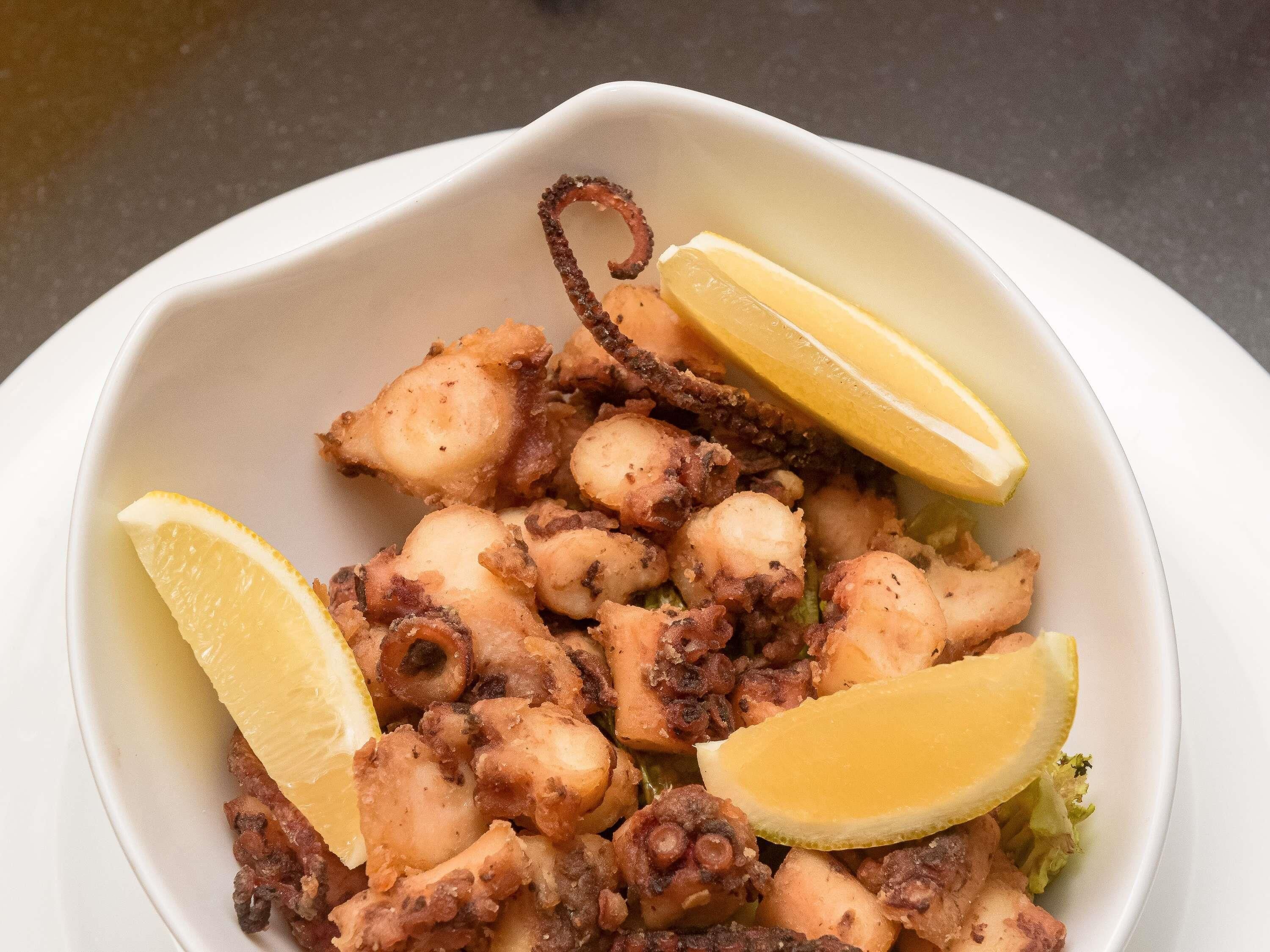 A bowl of octopus with lemon wedges.