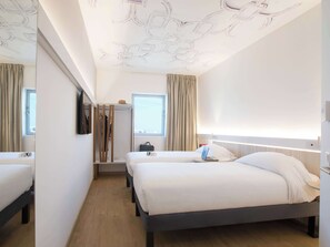 Two single beds with dark frames and white bedding, a large mirror, and a desk with a laptop and handbag.