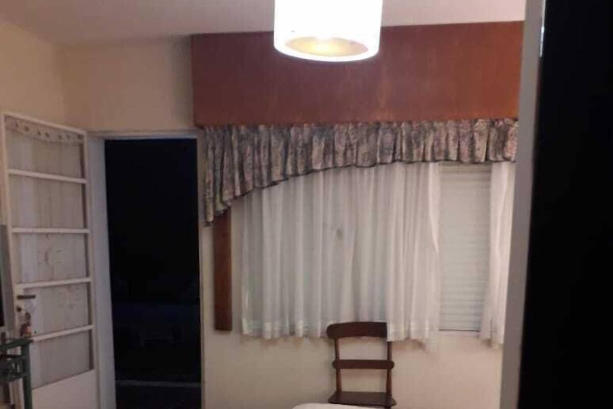 Une chambre à coucher avec un lit, une armoire, une chaise et une fenêtre avec des rideaux.