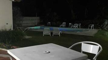 Un patio al aire libre con una mesa y sillas, una piscina y un edificio blanco al fondo.