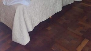 A hotel room with a bed, a bedside table, a lamp, and a door.