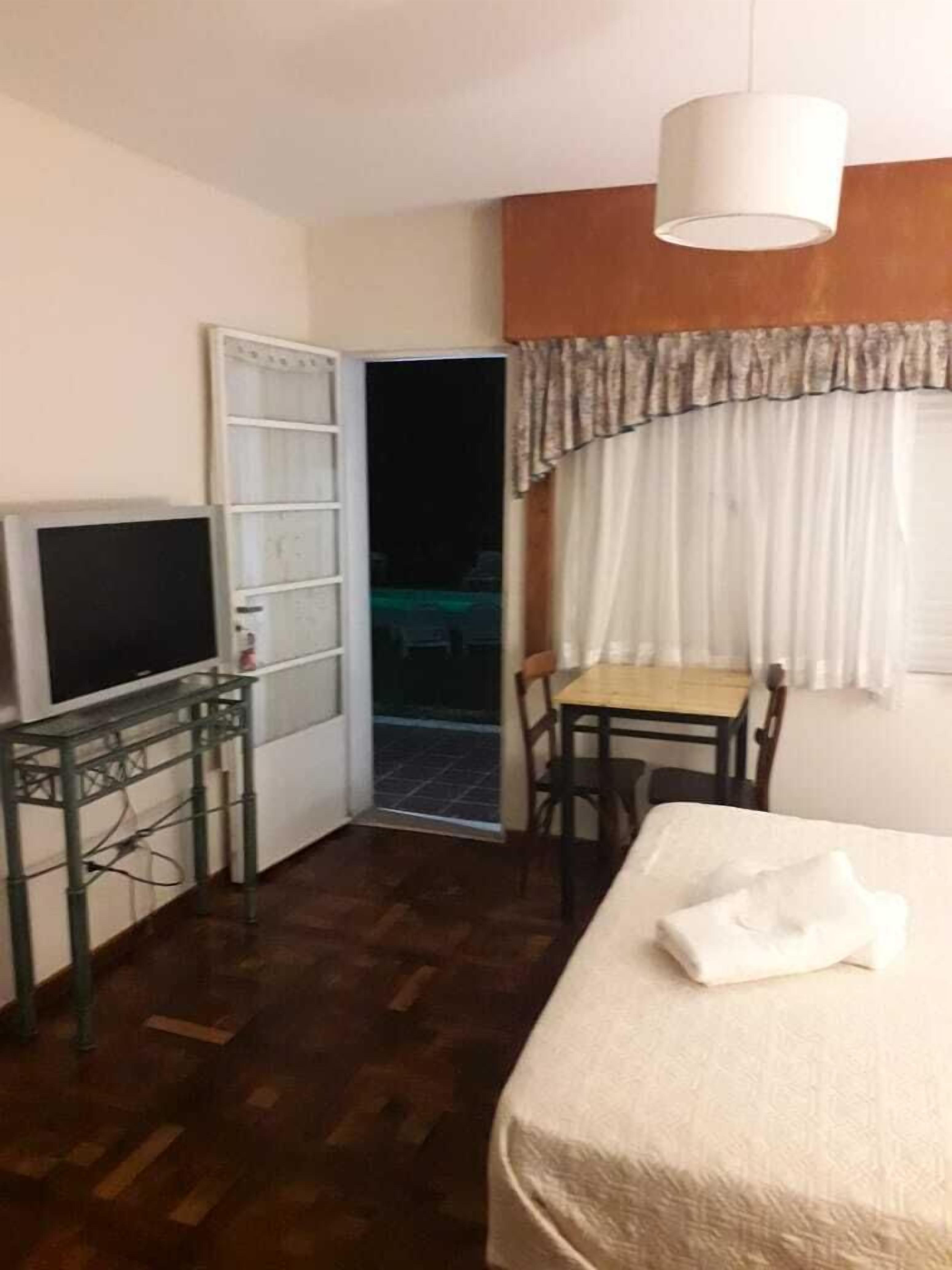 A hotel room with a bed, a desk with a chair, a television, and a door leading to an outdoor area.