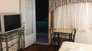 A hotel room with a bed, a desk with a chair, a television, and a door leading to an outdoor area.