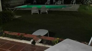 A nighttime view of a backyard with a swimming pool, several lounge chairs, and a patio table.