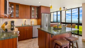 A modern kitchen with wooden cabinets, stainless steel appliances, and a large island with stools. - Oceanfront Two Bedroom Condo (Koloa)