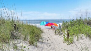 Een zandpad naar strandparasols en een bord.