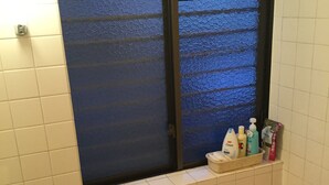 A bathroom with a window, a shelf with toiletries, and a bathtub. - Funabori Hasui (Tokyo)