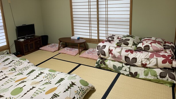 A traditional Japanese-style room with tatami flooring, a futon bed, a television on a wooden cabinet, and a shoji screen window. - Funabori Hasui (Tokyo)