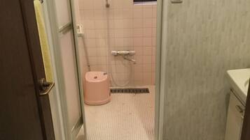 A bathroom with a shower, a toilet, and a bidet. There is a pink mat with Hello Kitty design in front of the toilet.