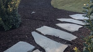 Ein angelegter Garten mit trittfesten Steinen, die zu einem Haus mit überdachter Veranda führen.