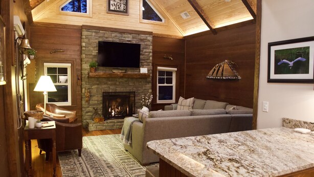 Ein gemütliches Wohnzimmer mit Kamin aus Stein, einer bequemen Couch und einem darüber montierten Fernseher.