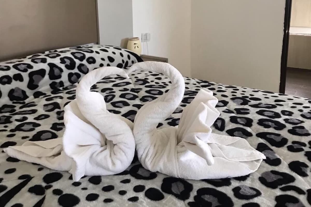 A bed with a leopard print cover and two swan-shaped towels placed on it.
