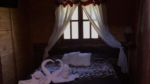 Una habitación de madera con una cama, cortinas blancas y una ventana.