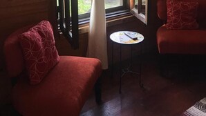 Una habitación acogedora con dos sillones tapizados en rojo, una mesita redonda y una ventana con cortinas.