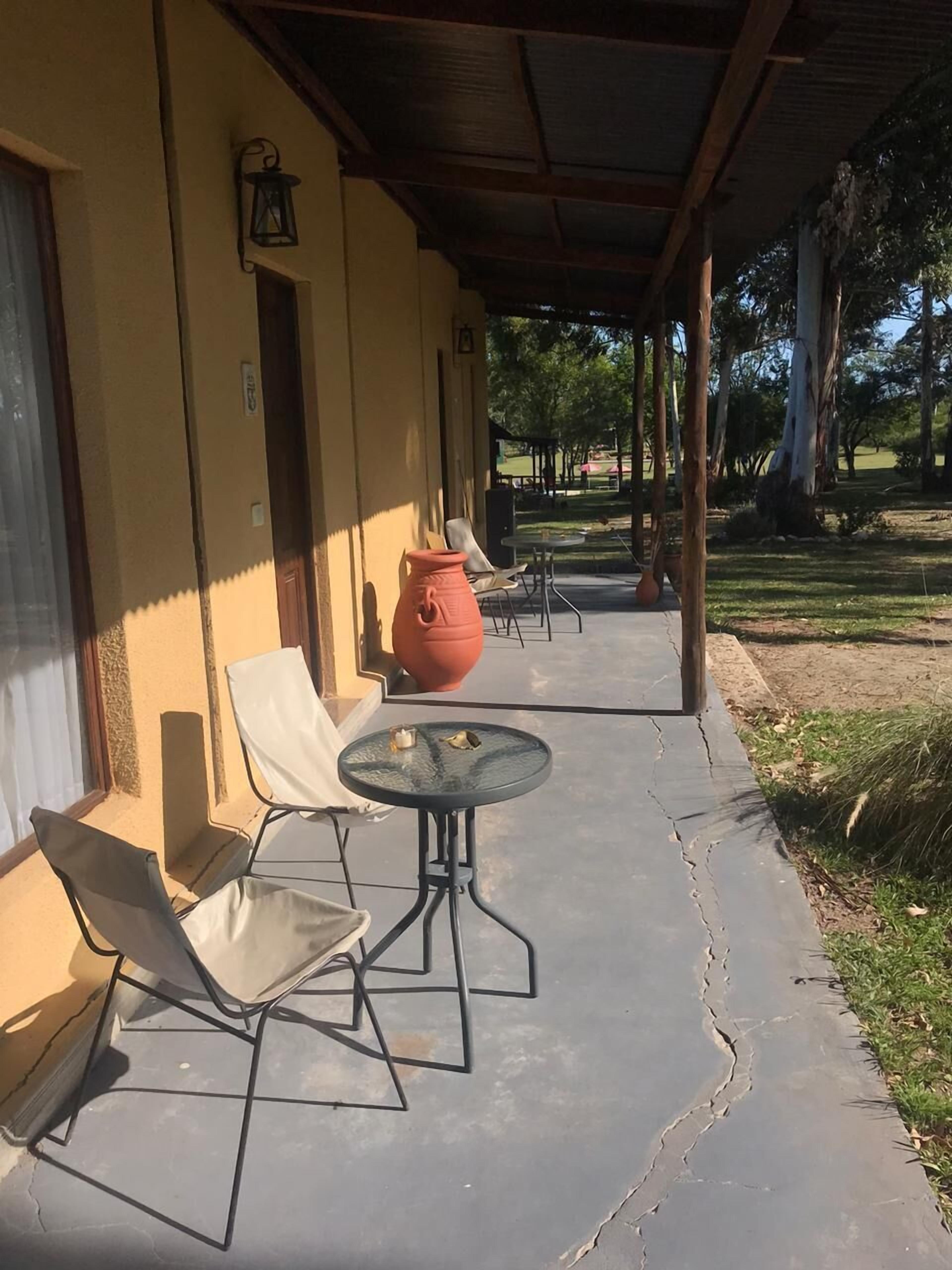 A covered patio with outdoor seating, a large terracotta pot, and a view of a park.
