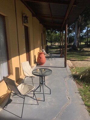 A covered patio with outdoor seating, a large terracotta pot, and a view of a park. - Posada Los Molles (Colon)