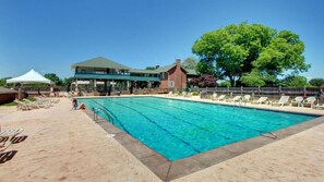 A swimming pool with lounge chairs and a covered area, surrounded by buildings and a large tree.