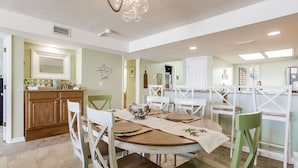 A dining area with a round table, white chairs, and a kitchen in the background. - Orange Beach Gulf-Front 2BR • Sleeps 7 • 2 La-Z-Boy Recliners • Pools • Boats (Orange Beach)
