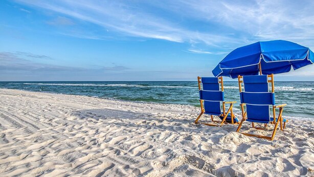 Two blue beach chairs and a blue umbrella on a sandy beach with the ocean in the background. - Orange Beach Gulf-Front 2BR • Sleeps 7 • 2 La-Z-Boy Recliners • Pools • Boats (Orange Beach)