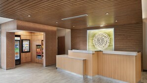 A reception area with a wooden reception desk, a refrigerator stocked with beverages, and a wall-mounted decorative piece. - Fairfield Inn & Suites by Marriott Tampa Riverview (Riverview)
