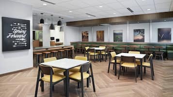 Um restaurante moderno com piso de madeira, cadeiras amarelas e castanhas, e uma área de assentos em um estante verde.