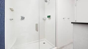 Un baño moderno con ducha acristalada, azulejos blancos y un pequeño estante con artículos de aseo.