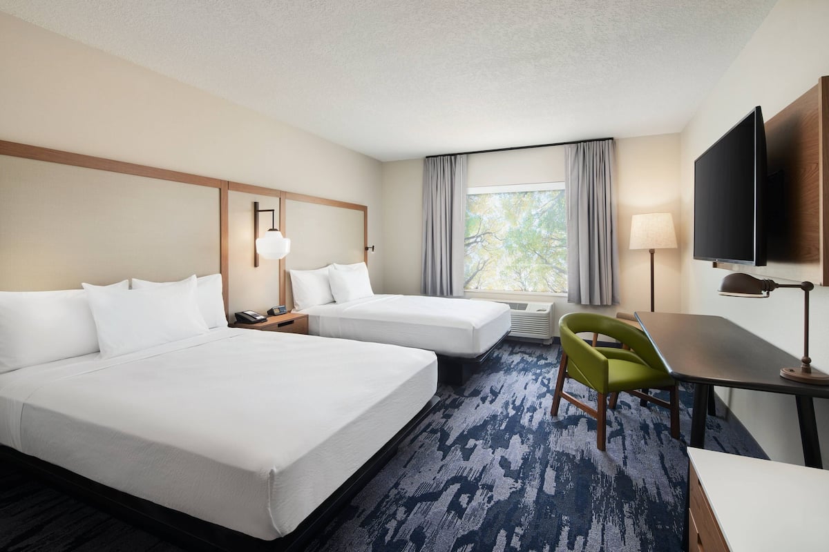 A hotel room with two beds, a desk, a chair, a TV, and a window with curtains.