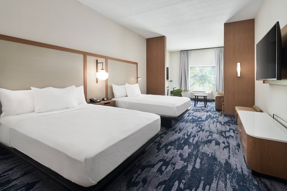 A hotel room with two beds, a desk, a chair, a TV, and a window with curtains.