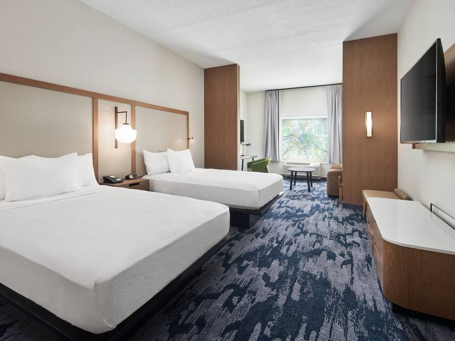 Una habitación de hotel con dos camas, un escritorio, una silla, un televisor y una ventana con cortinas.