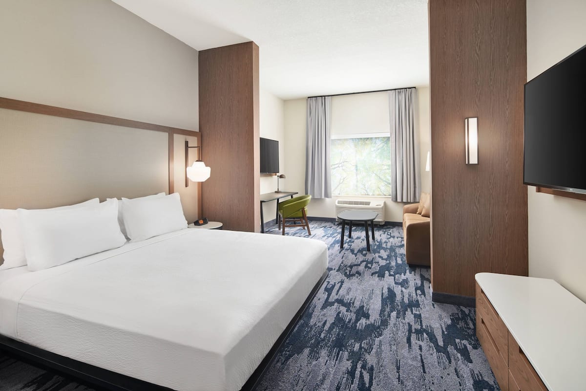 A hotel room with a large bed, a desk, a chair, a TV, and a window with curtains.
