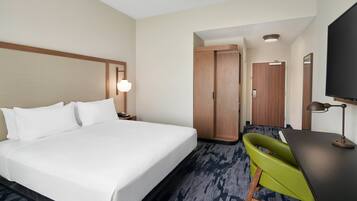 Una habitación de hotel con una cama grande, un escritorio con una silla, un televisor y un armario.