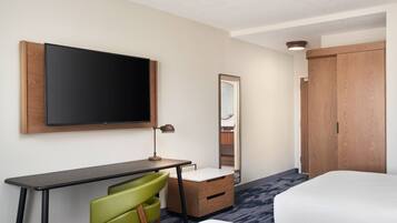 Una habitación de hotel con cama, escritorio con silla, televisor, espejo y armario.