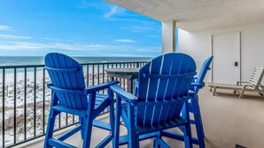 A balcony with two blue Adirondack chairs and a table, overlooking a beach with a clear view of the ocean. - Orange Beach Gulf View 2BR • Sleeps 6 • 2 Pools • Beach • Boat Slips (Orange Beach)