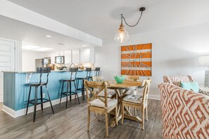 A modern kitchen with white cabinets, a blue accent wall, and a dining area with wooden chairs and a table.