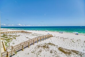 A beach with a wooden boardwalk, sandy dunes, and a clear blue ocean.