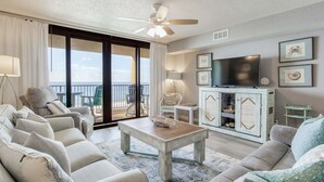 Un salon comprenant un canapé, des fauteuils, une table basse, un téléviseur et un balcon avec vue.