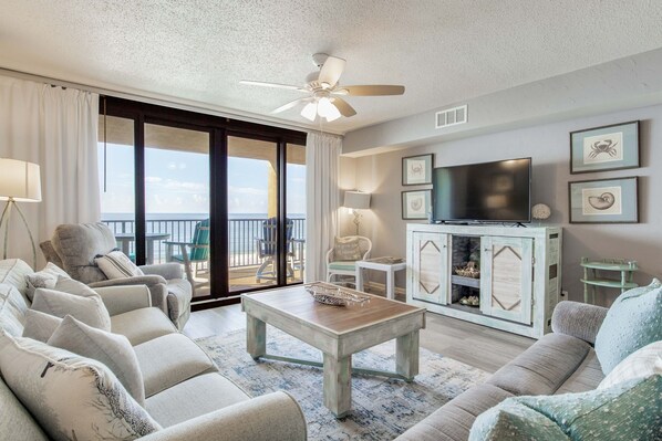 A living room with a sofa, armchairs, a coffee table, a TV, and a balcony with a view.