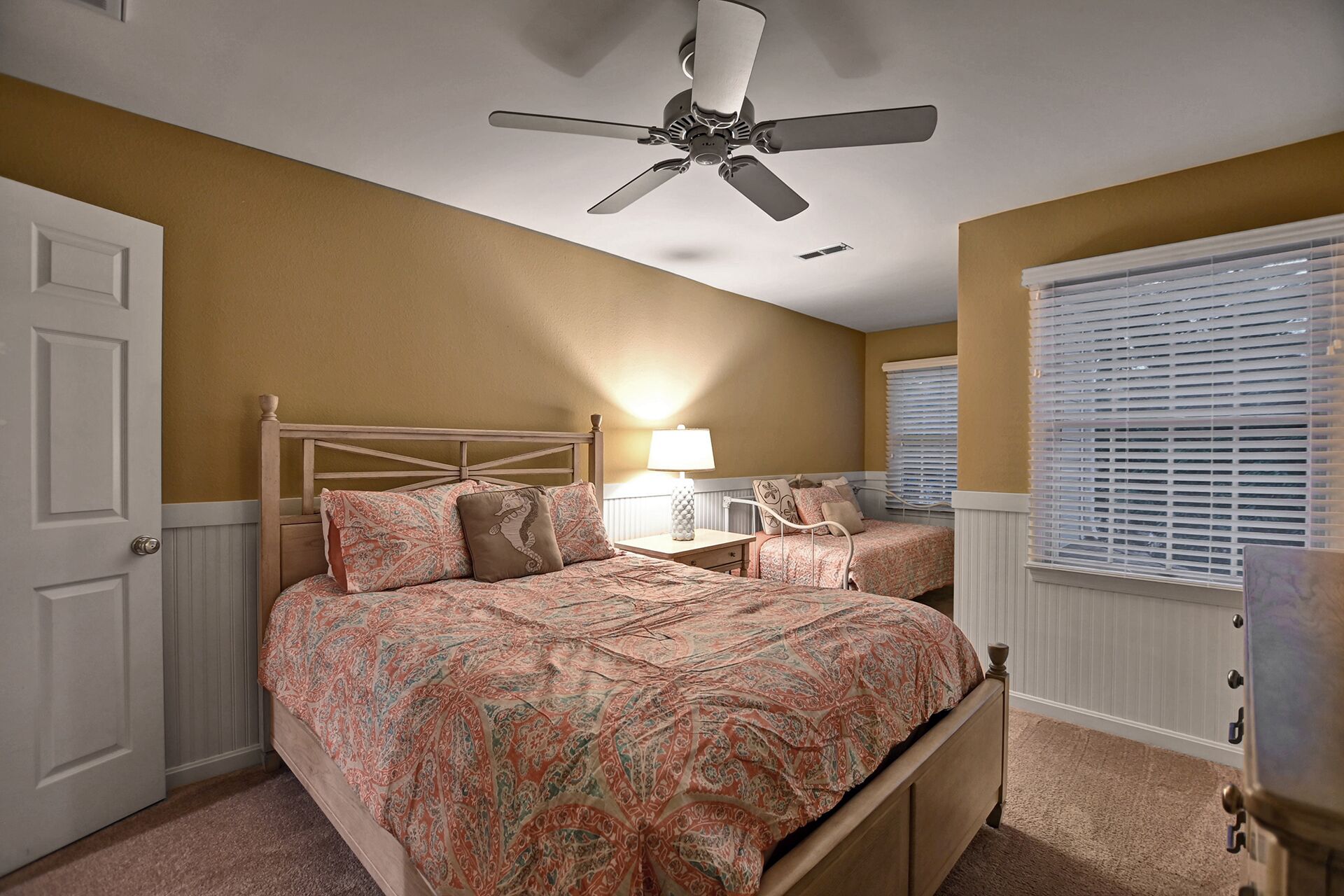 A bedroom with a bed, a nightstand, a lamp, a ceiling fan, and a window with blinds.