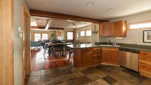 A spacious kitchen with wooden cabinets, a central island, and a dining area with a large table and chairs. - Second Street Stay–Downtown+ WALKABLE TO CHERRY FEST (Traverse City)