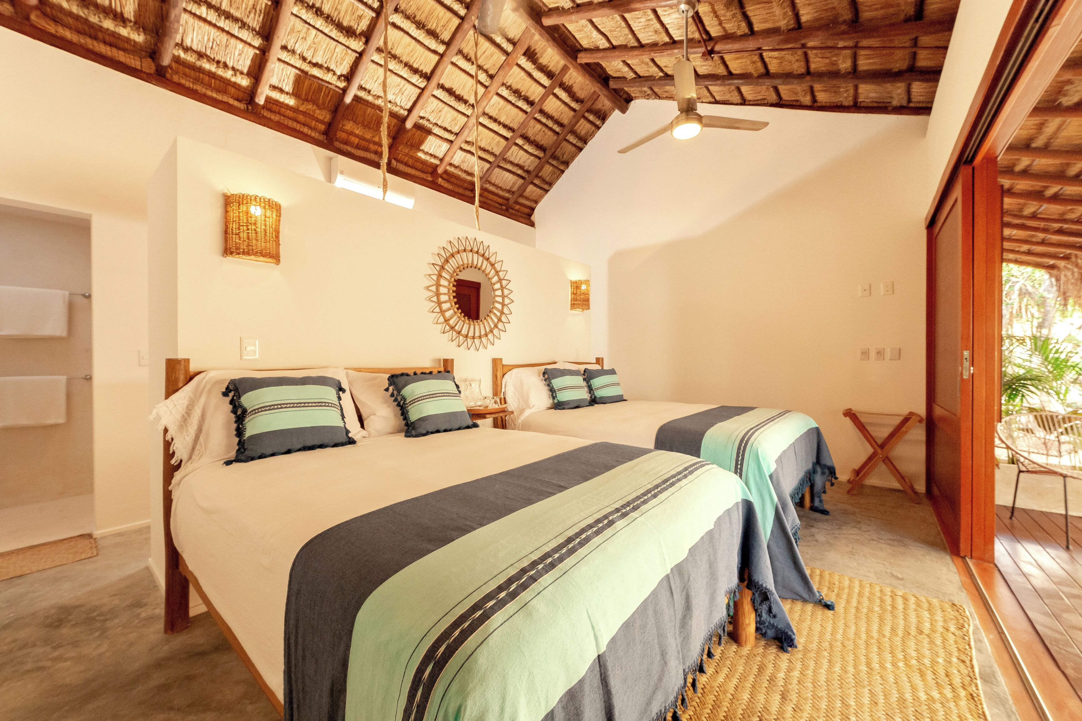 A room with two beds, a ceiling fan, a woven mat, and a view of the outdoors.