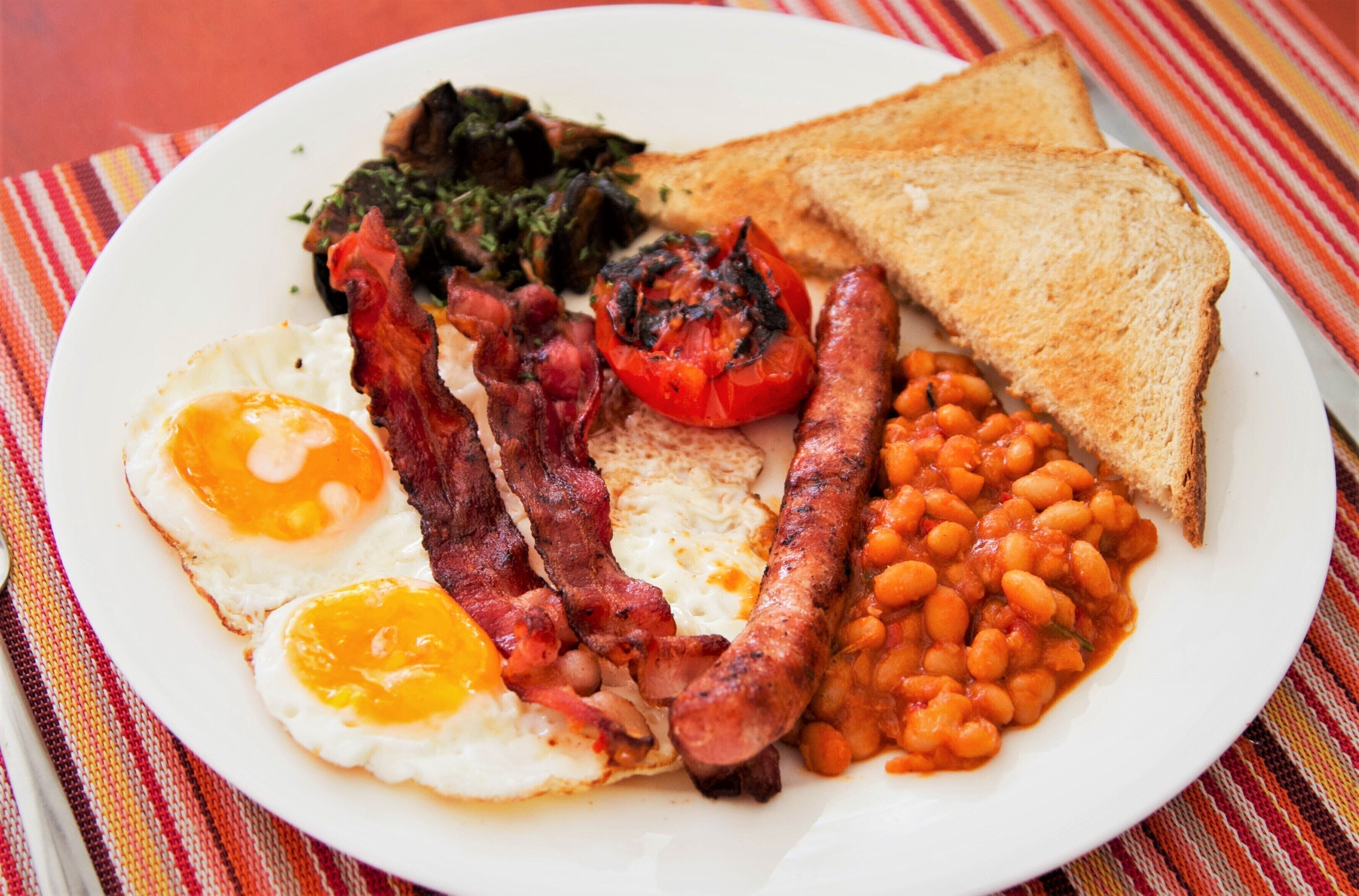 A plate of breakfast food including eggs, bacon, sausages, toast, beans, and tomatoes.