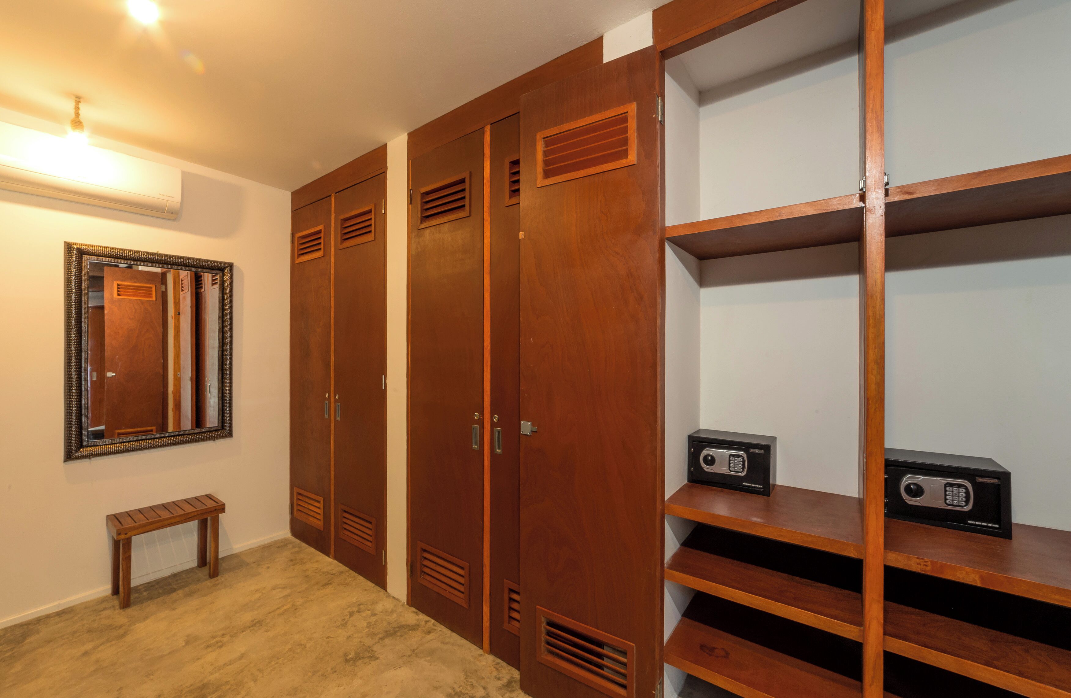 A room with wooden wardrobes, a bench, and a shelf with electronic devices.