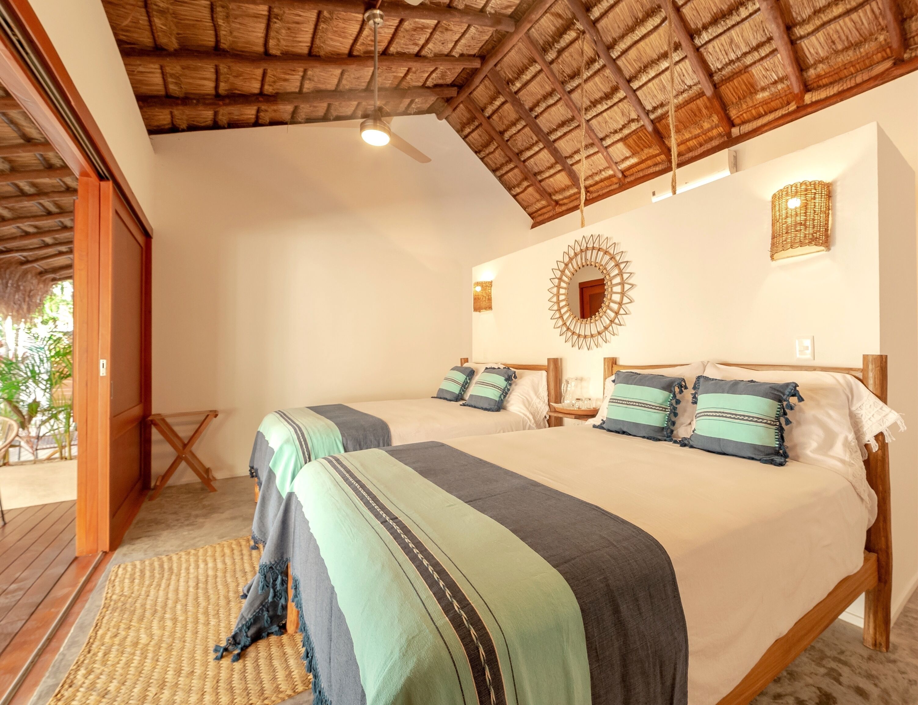 A room with two beds, a wooden ceiling, a woven mat, and a decorative mirror.