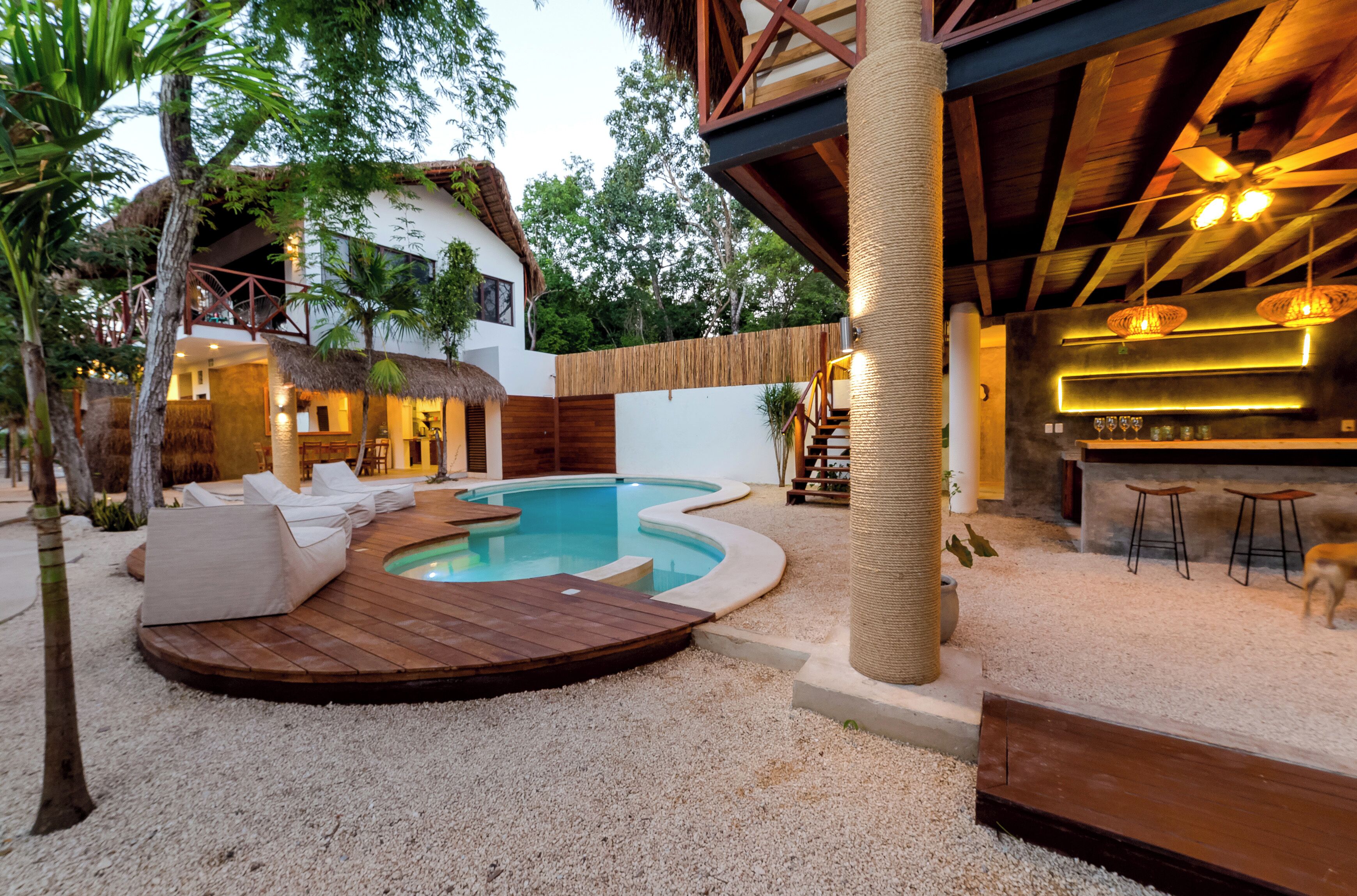 A pool area with a wooden deck, lounge chairs, and a bar area with stools.