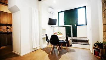 Un ambiente compatto con zona pranzo, televisione a parete, una porta verde e una scala che conduce a un livello superiore.