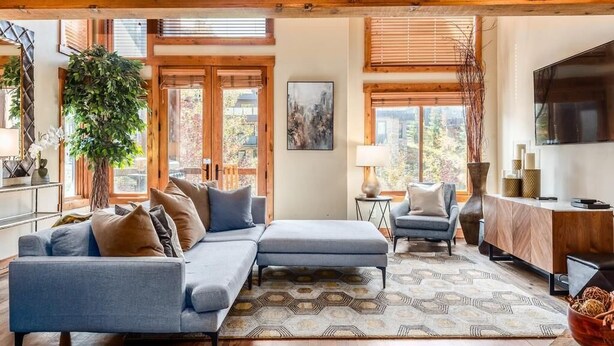 A modern living room with a sectional sofa, a small side table, a lamp, and a large window with blinds.