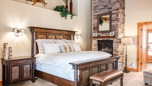 A bedroom with a large bed, a stone fireplace, and a wooden bench.