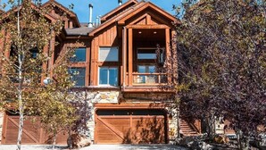 A two-story wooden house with a garage, large windows, and a stone foundation.