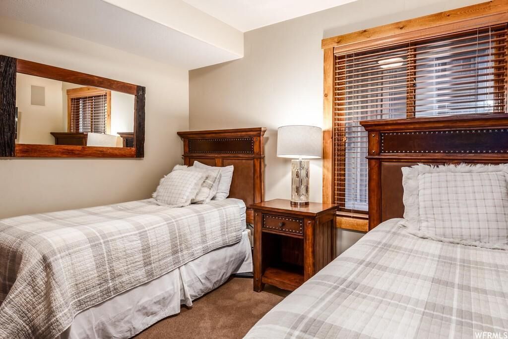 Habitación de hotel con dos camas, una mesita de noche, un espejo y una ventana con persianas.