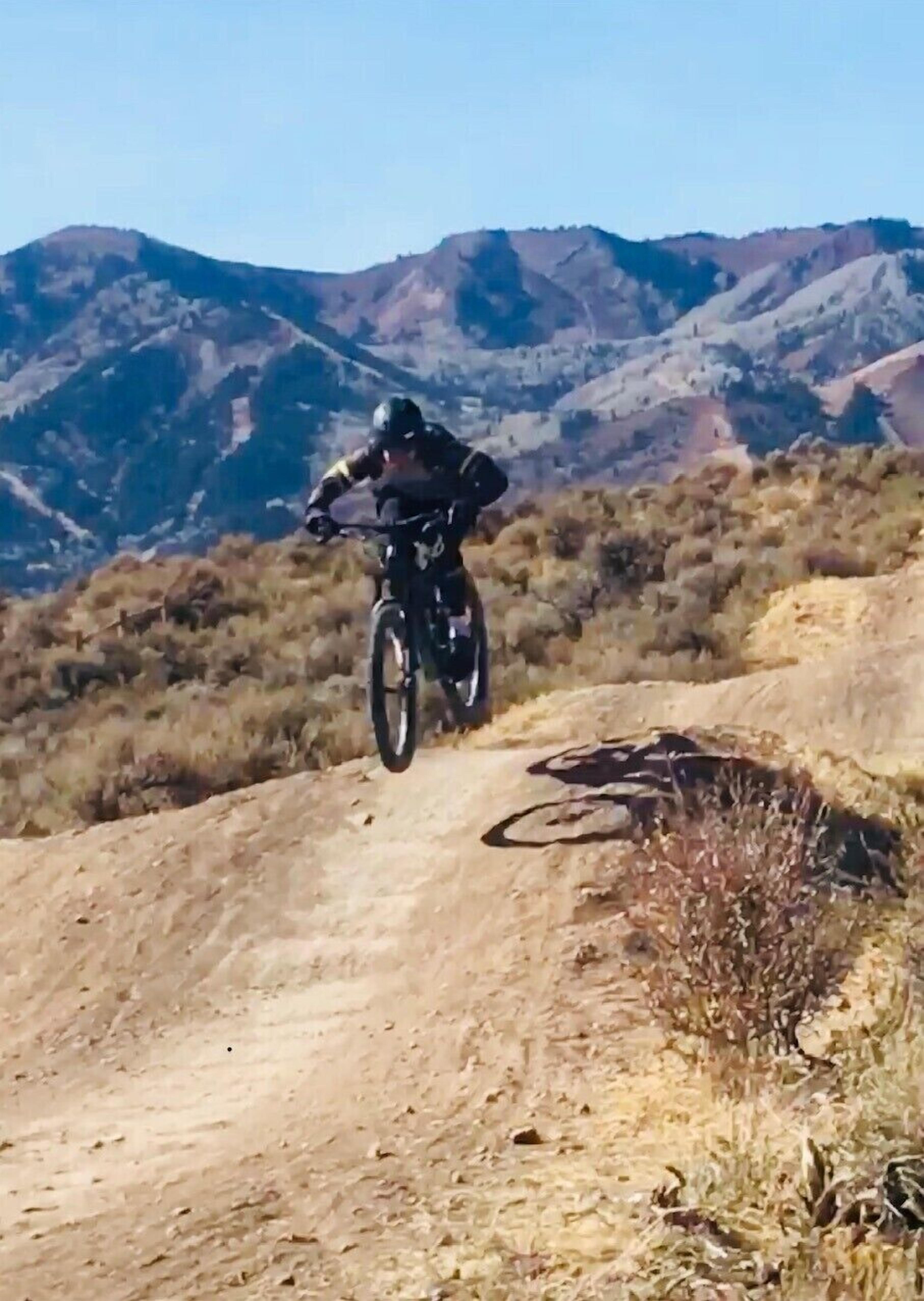 A person on a mountain bike on a dirt path with a mountainous landscape in the background.